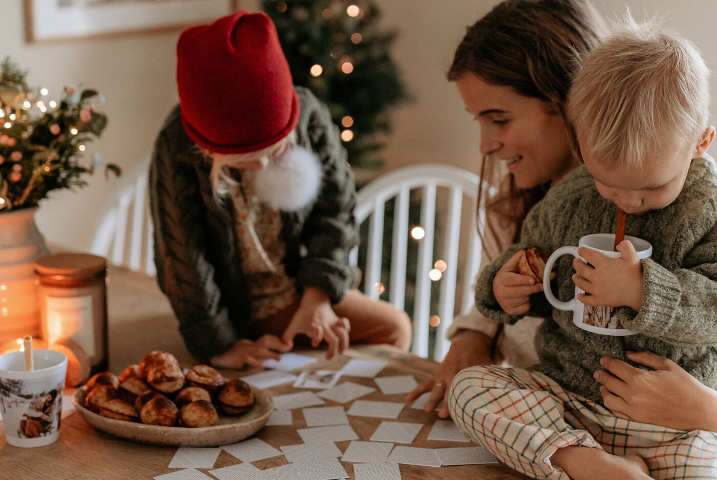 En familie laver et kreativt projekt sammen ved et bord omfavnet af småkager og en varm juleatmosfære.