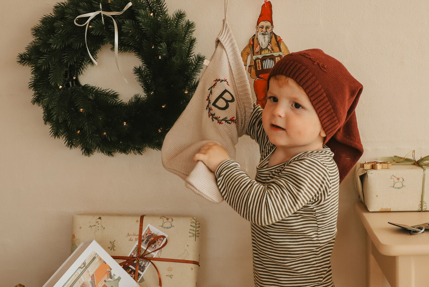 Et barn hænger en julestrømpe op på en væg med en krans.