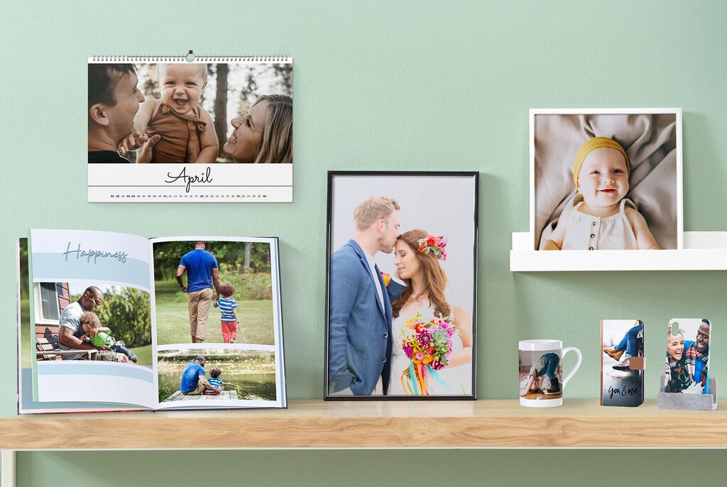 Et stilfuldt bord med forskellige fotoprodukter: en kalender, et indrammet billede, et fotobog og en kop med kreative minder