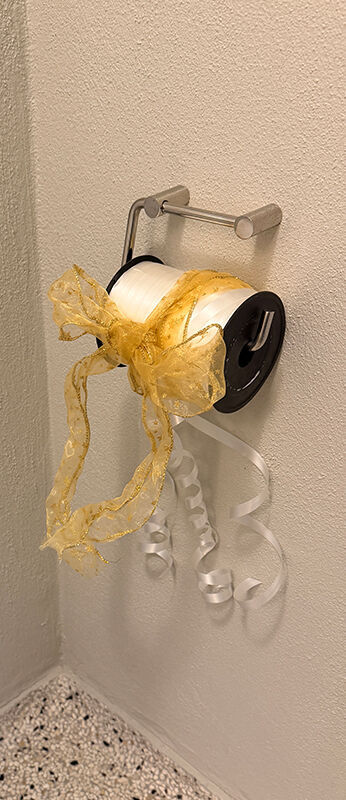 En rulle gave bånd i hvid og guld hænger på en holder til toiletpapir.